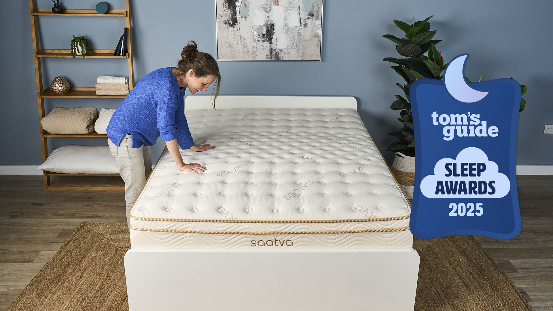 A Saatva Classic mattress in a bedroom, with a woman pressing her hands down on it and a Tom&#039;s Guide Sleep Awards 2025 badge overlaid