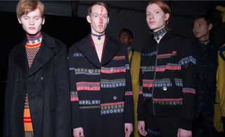 2 male models in matching coats, 1 with ink on his face