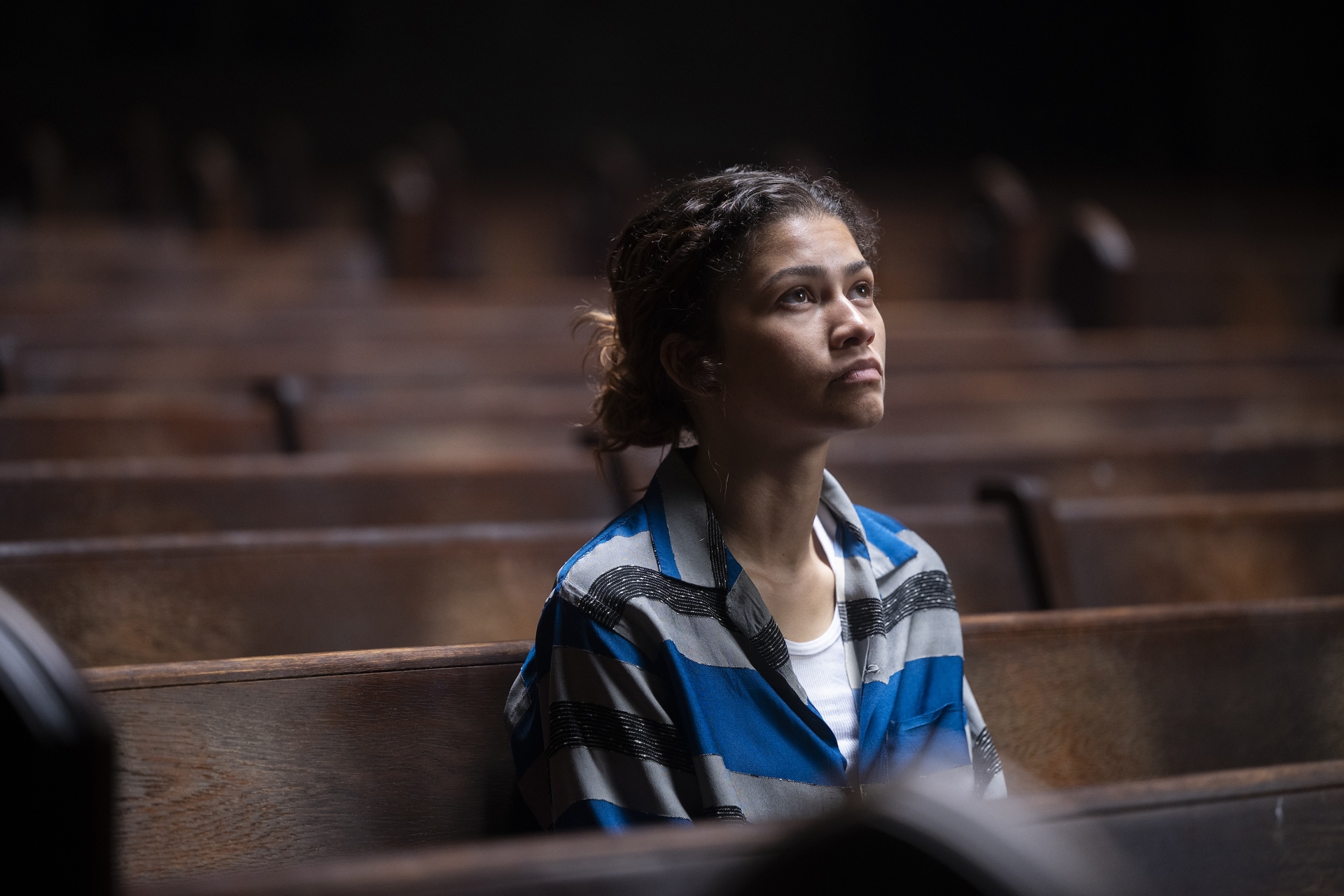 zendaya as rue wearing a blue striped shirt sitting in a pew in an empty church in euphoria season 3