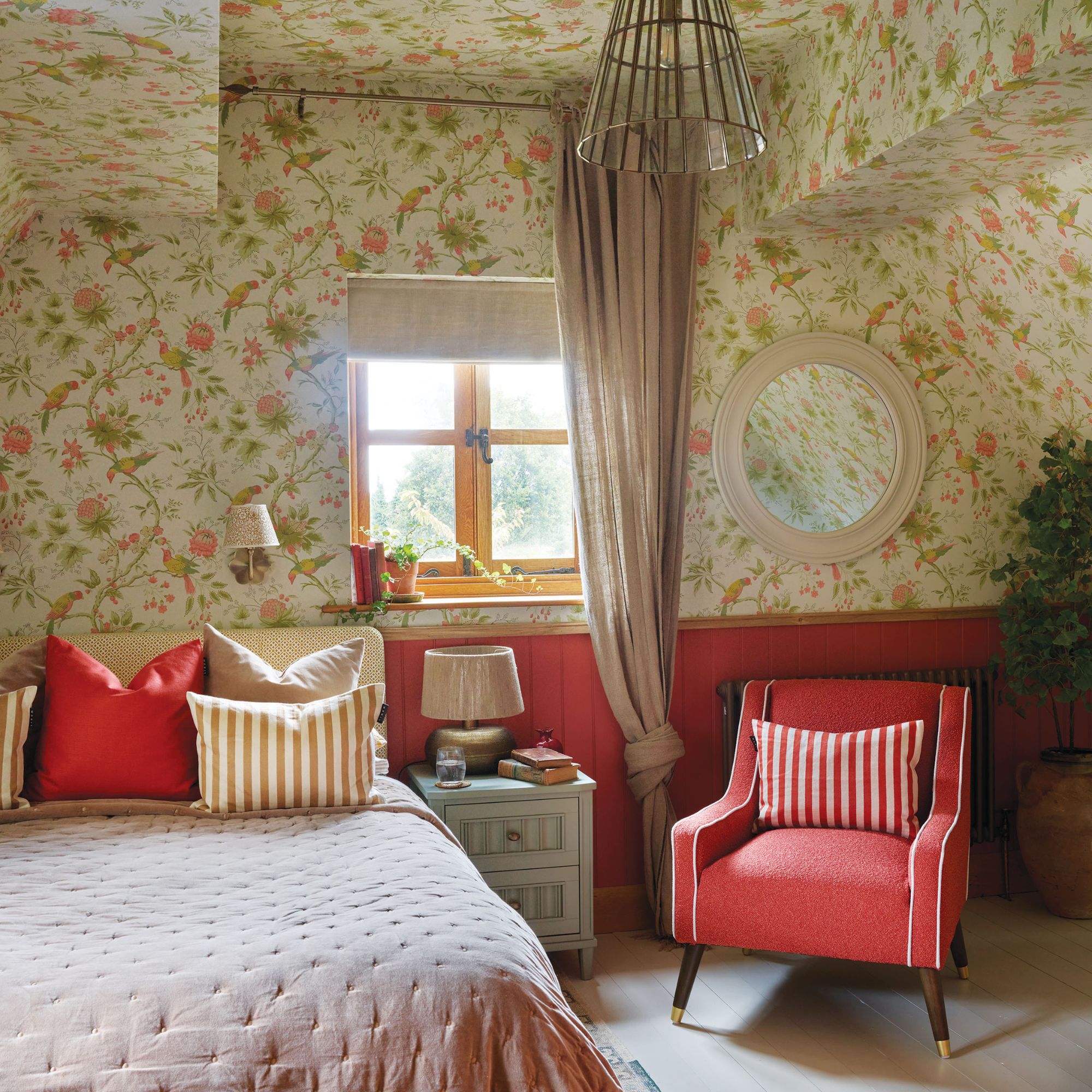 Bedroom with floral wallpaper and red panelling, with red armchair and colourful bed