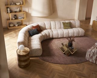 Living room with wooden floors, round rug, and pink curved sofa
