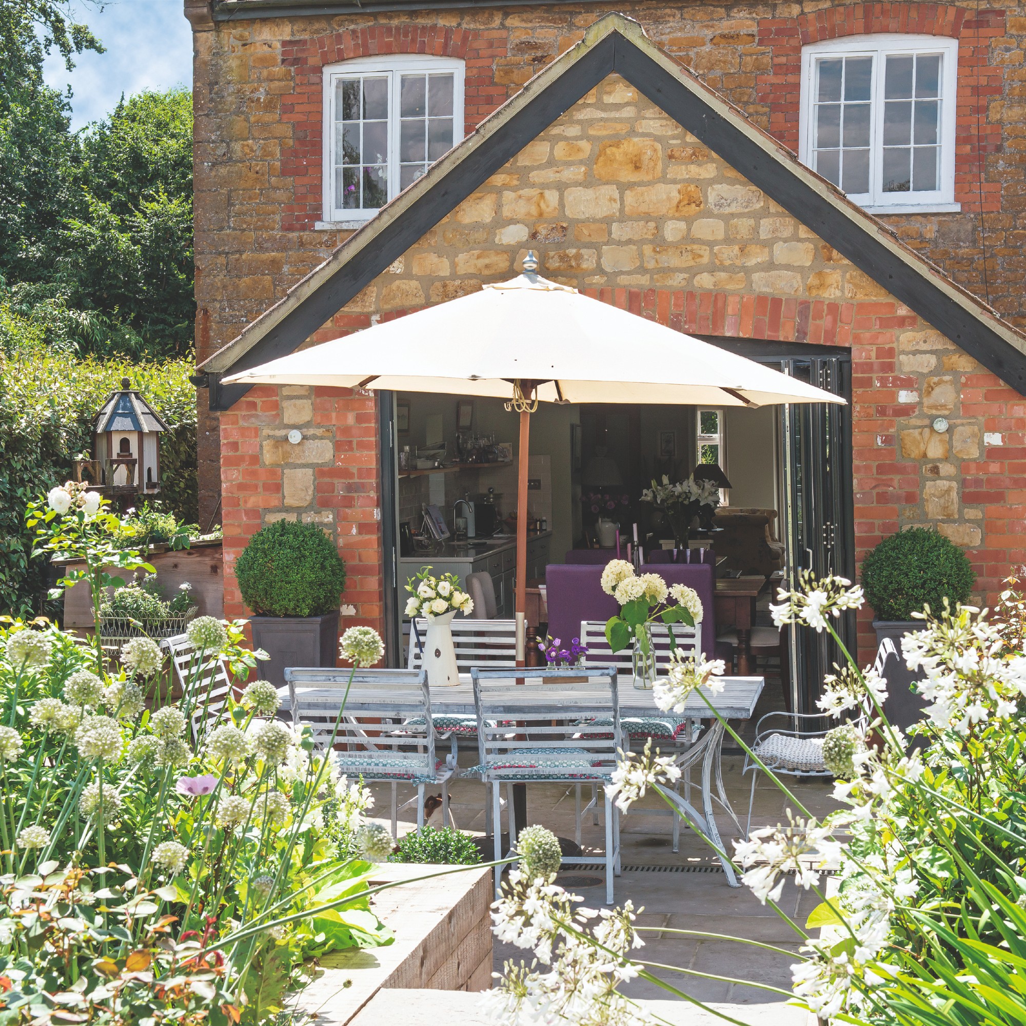 A small garden with a metal dining set and a cream parasol in the middle