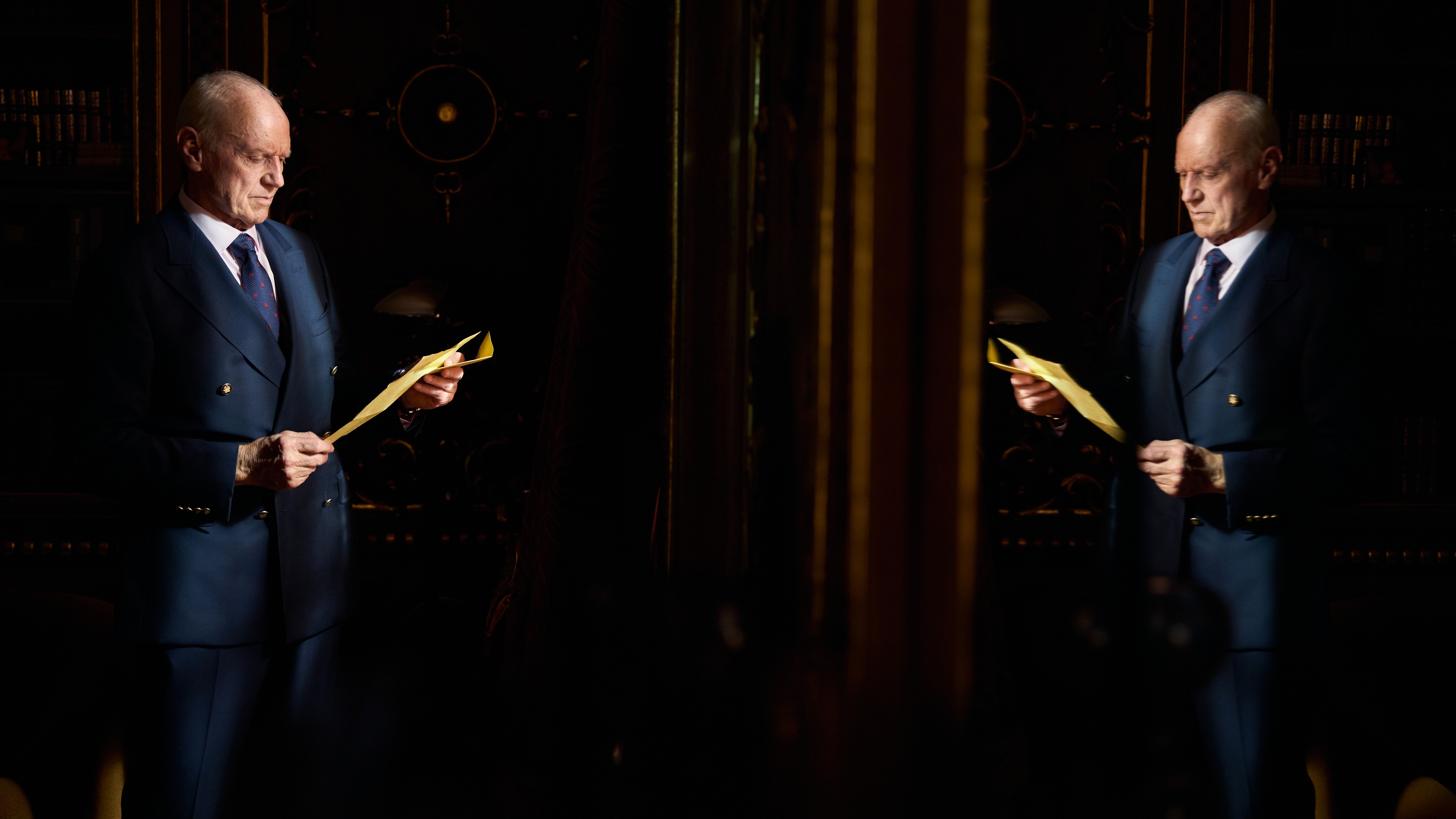 Aaron reading a letting in a dark room, and his image is reflected in a mirror.