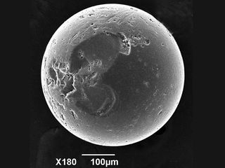 A scanning electron microscope image of a glass bead with divots and scratches. The heat of the explosions during the battle appears to have melted iron and even quartz in the sand, creating beads like this one.