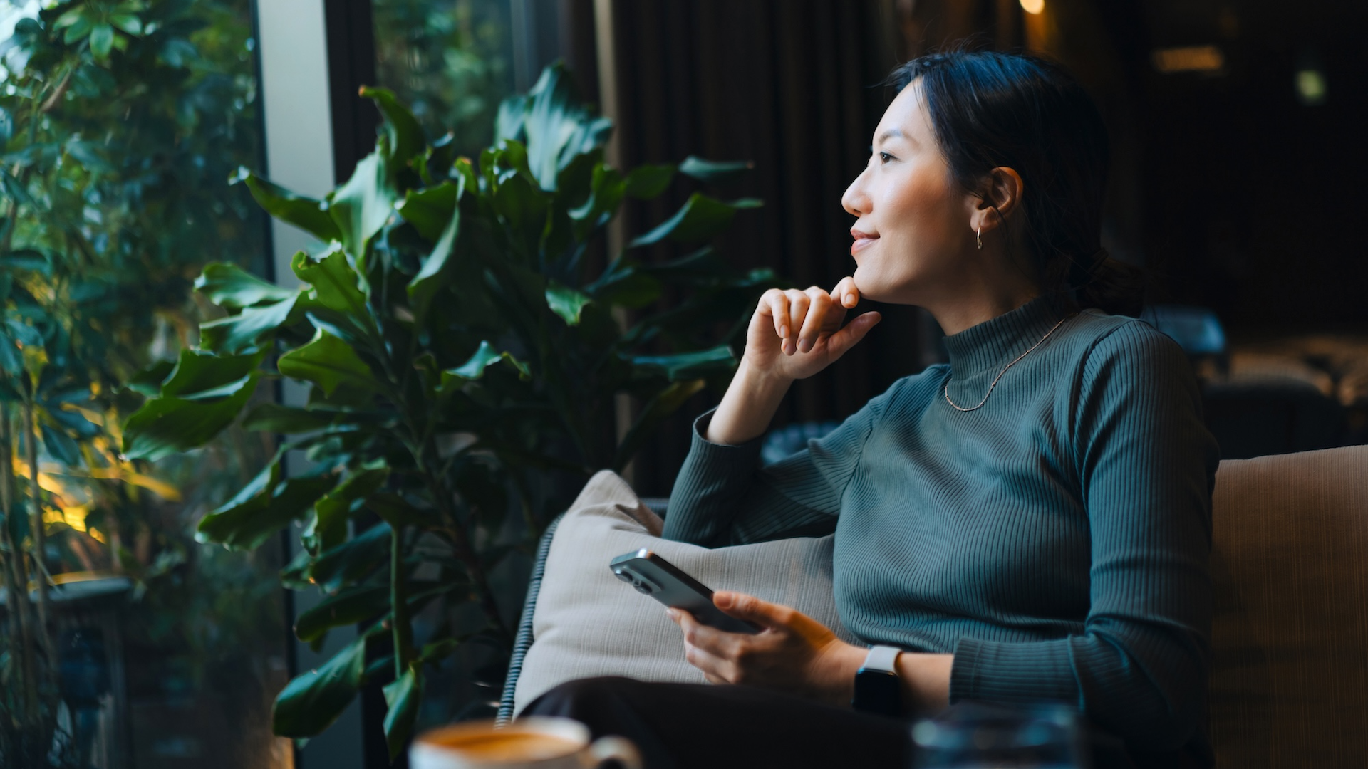 Woman looking out of window while holding phone