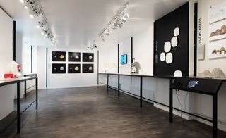 An art display room featuring white walls and ceiling with dark wood flooring. Milk art display on the shelves and walls of the room