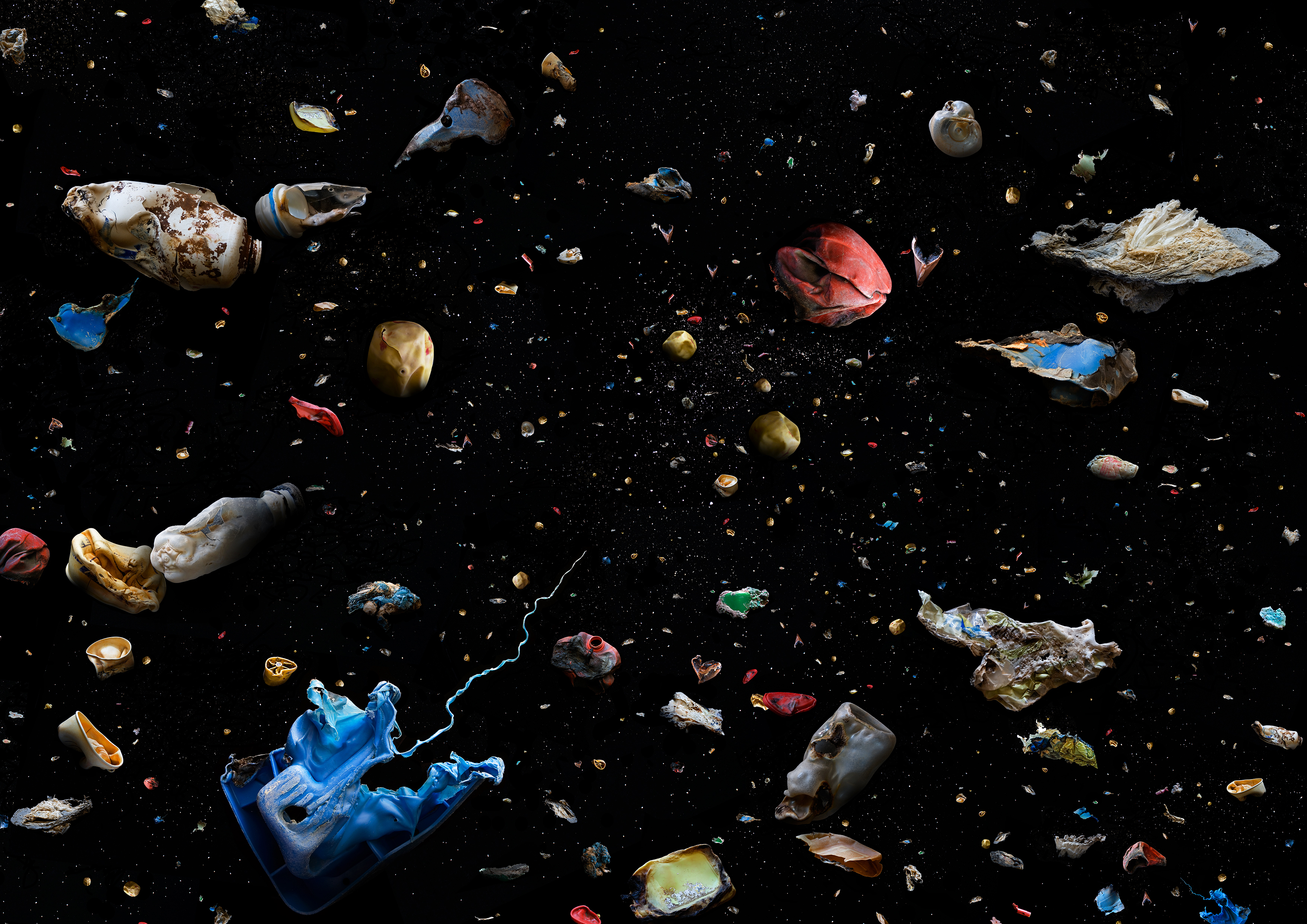 Plastic oceanic debris appears colorfully in sharp contrast against the pitch black of the ocean, items include a toothpaste tube and other recognizable waste