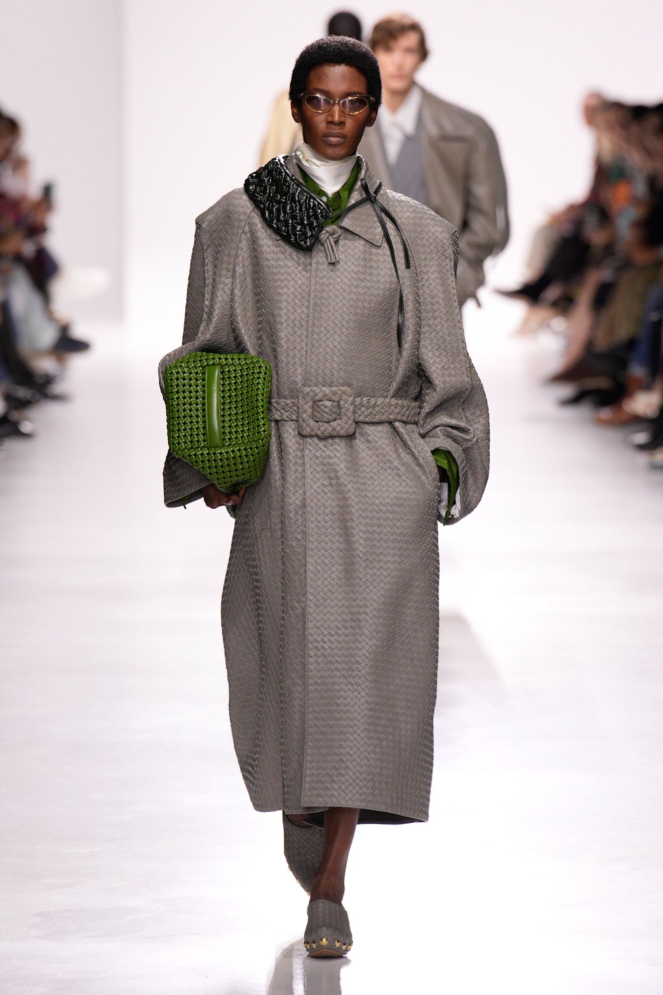 A model walking in the S/S 26 Bottega Veneta show wearing a gray Intrecciato trench coat.