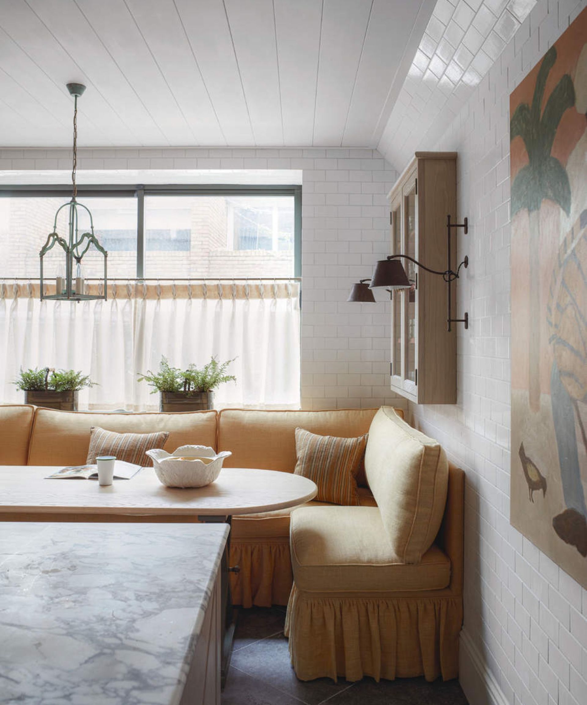 A yellow sofa in the corner of a kitchen against white walls and the corner of a white marble counter.