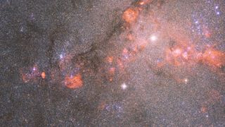 hubble telescope photo of a star-packed galaxy filled with orange-red clouds of gas