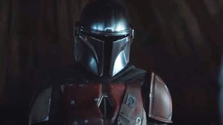 Din looking at his bounty in The Mandalorian. He's wearing a helmet and a leather chest piece