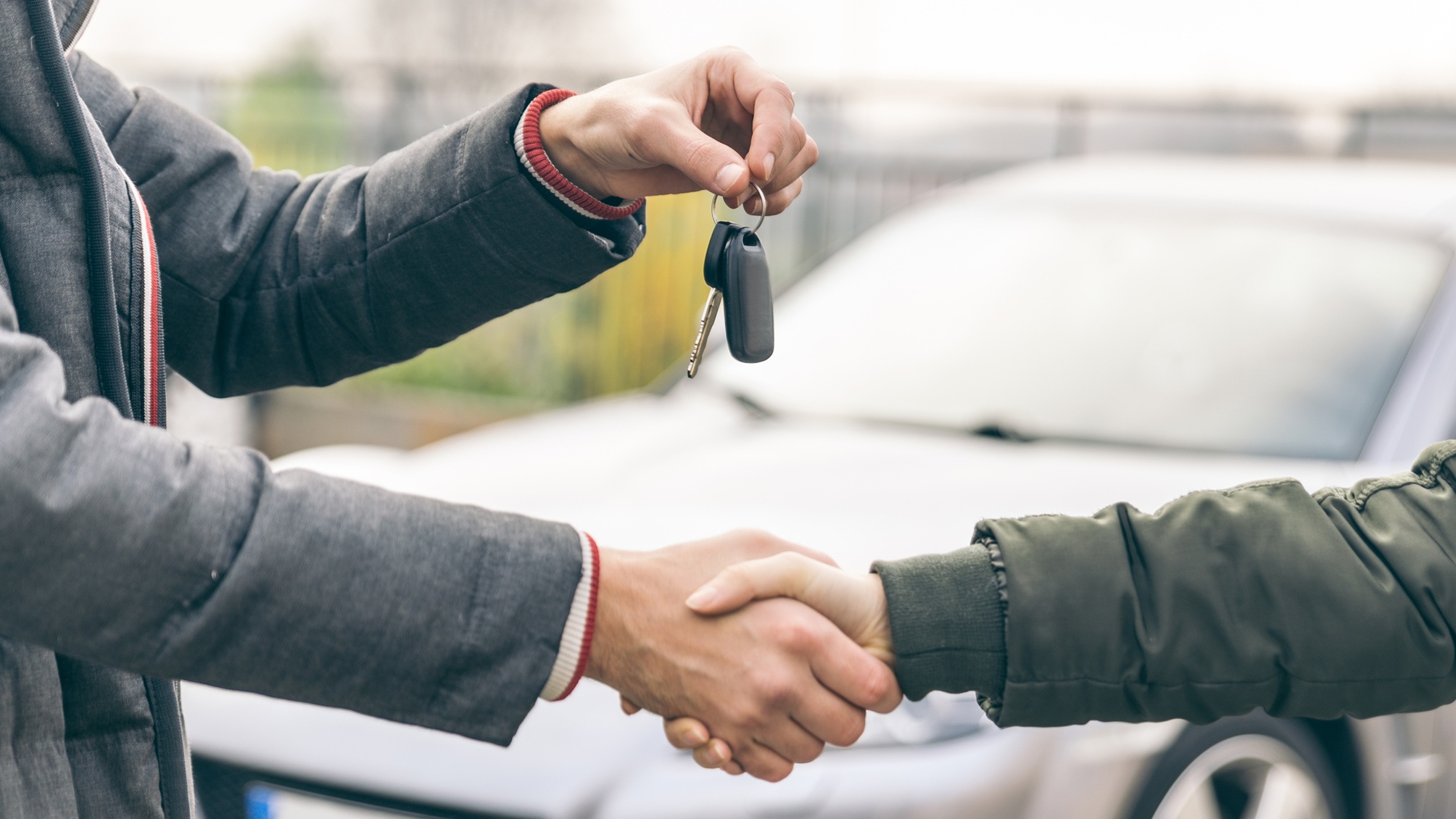 A car dealer hands over the keys to a new car and shakes the buyer's hand.