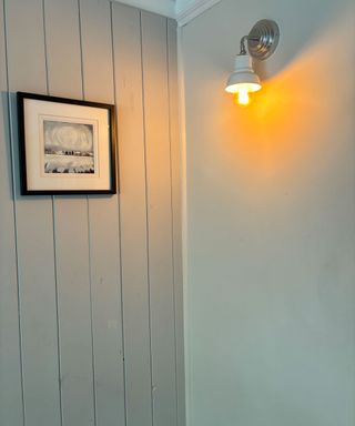 corner of a room with grey wall paneling and cream wall light