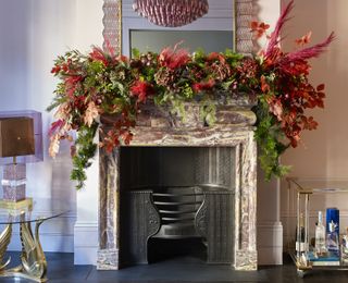 A fireplace decorated with a pink and green Christmas garland to match a pink stone fire surround