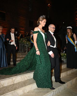 Princess Madeleine wearing a green sparkling evening gown with a long train walking on the arm of a man down a staircase