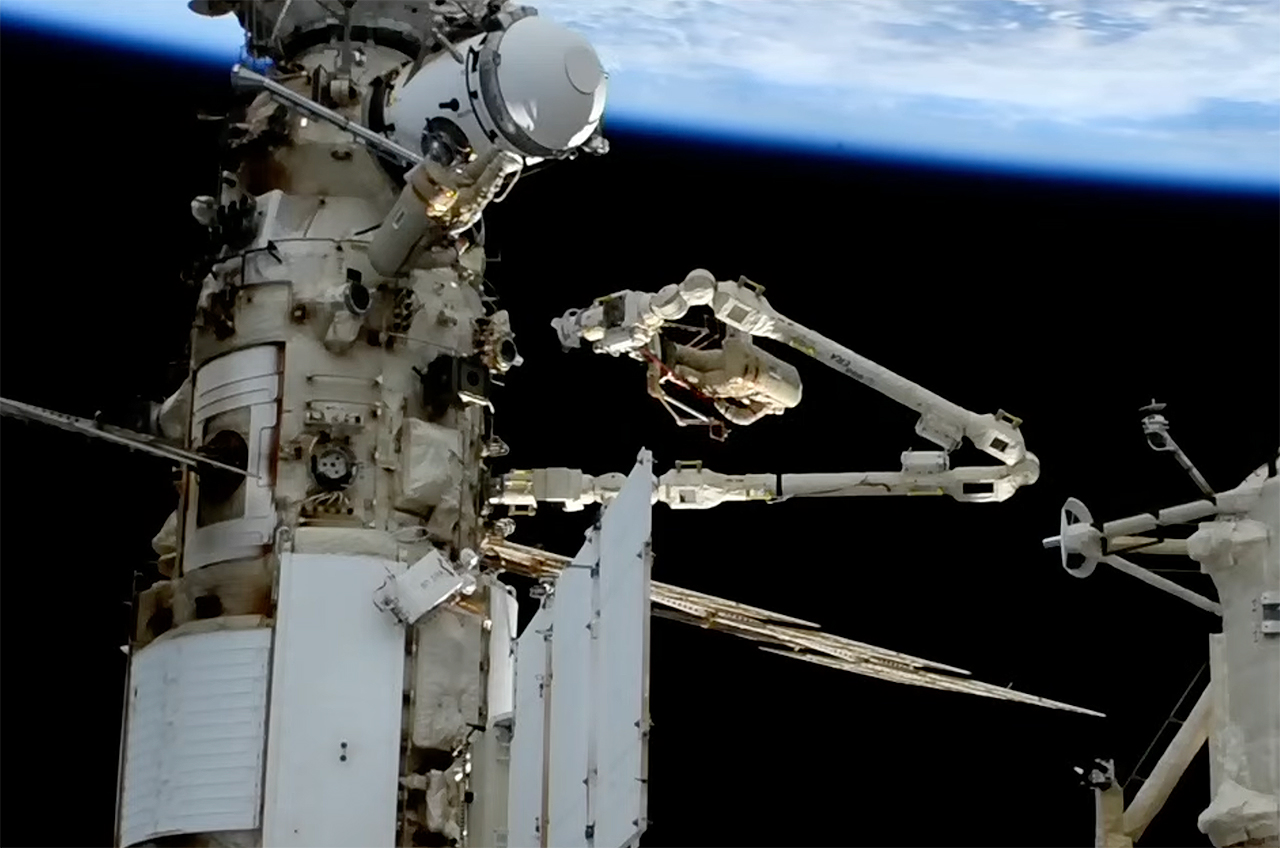 an astronaut on a spacewalk works at the end of a long robotic arm outside the international space station