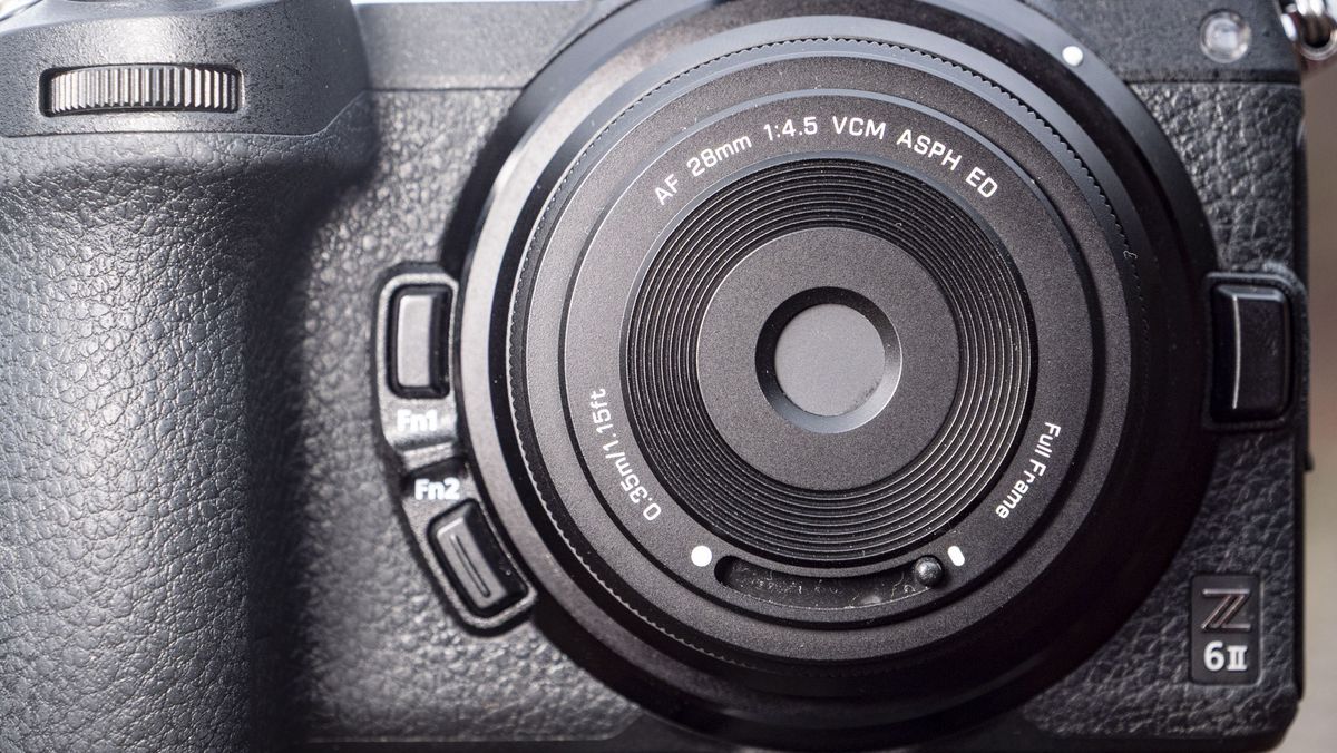 Closeup of the Viltrox AF 28mm f/4.5 body cap lens, protector covering the lens