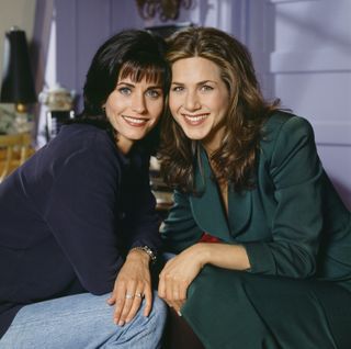 Courteney cox and jennifer anniston as monica and rachel leaning in for a posed photo in the apartment in friends