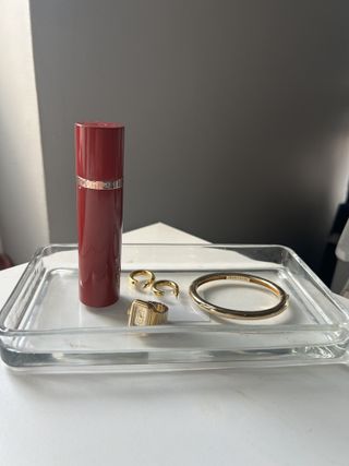 Bottle of travel size Tom Ford Lost Cherry perfume sitting on glass tray with gold bangle, ring, and hoop earrings