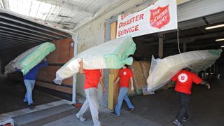 People wearing red t-shirts and jeans moving packed mattresses to the Salvation Army disaster donation service space