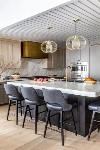 A kitchen with a large marble island, globe pendant lamps, and blue bar stools