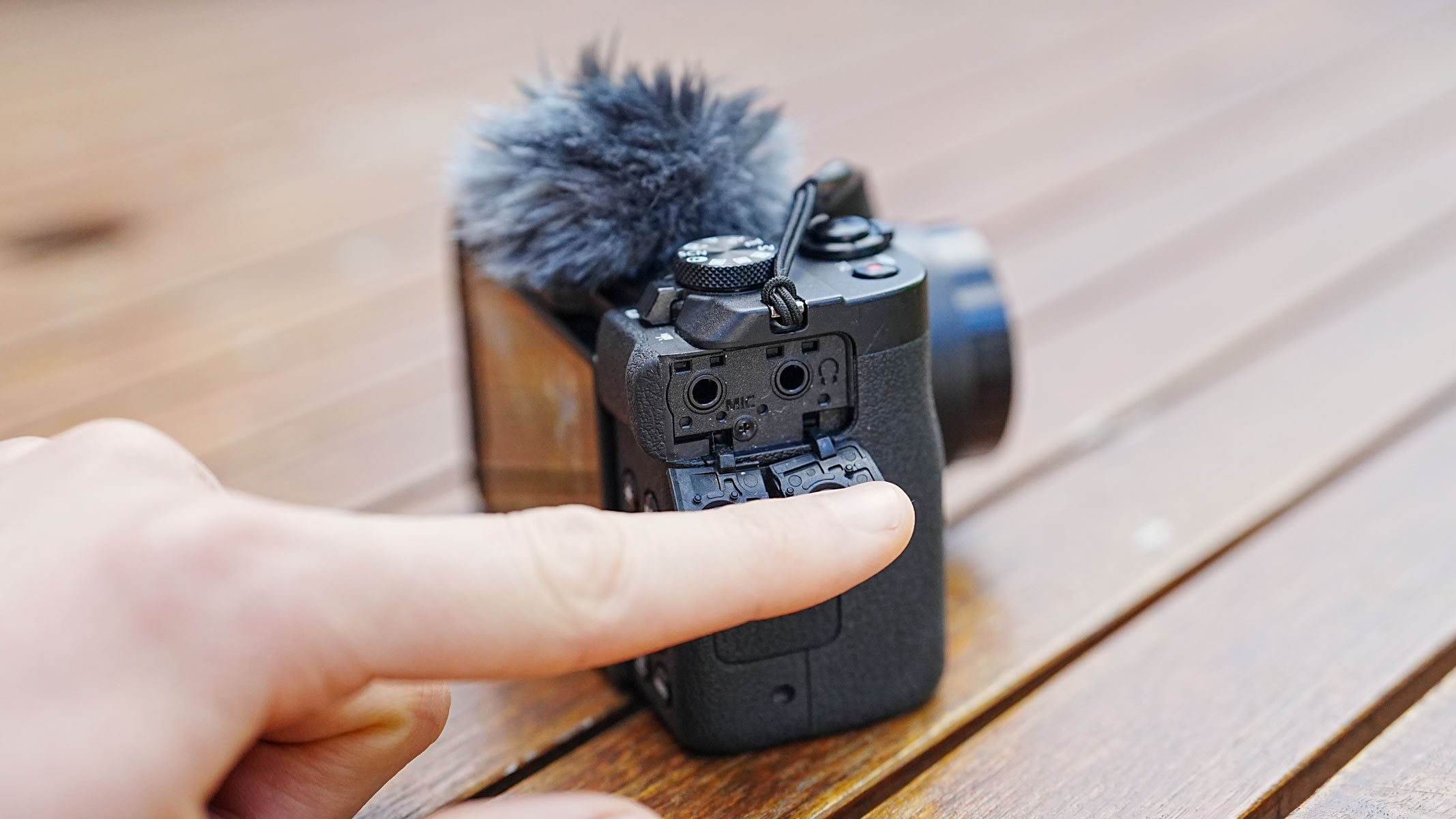 The Canon Powershot V1 on a wooden table with side cover open showing 3.5mm cable jacks.