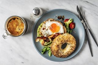 PCOS treatment: Bagel sandwich with avocado, fried egg and side salad on white background
