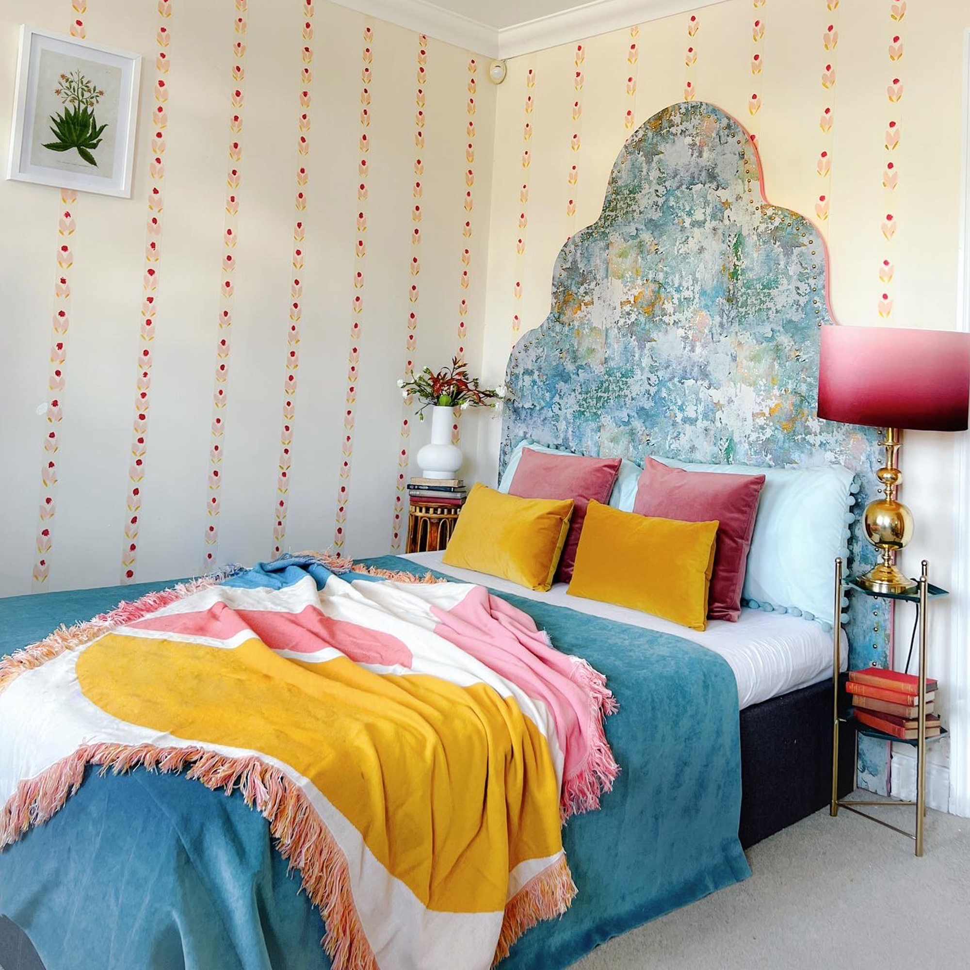 bed with large blue headboard in a beige room with pink stripes
