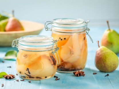 Two jar of preserved pears sit next to several whole pears and seeds