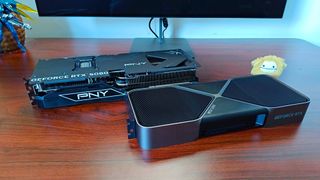 PNY RTX 5080 OC next to Founder Edition lying fat on woodgrain desk