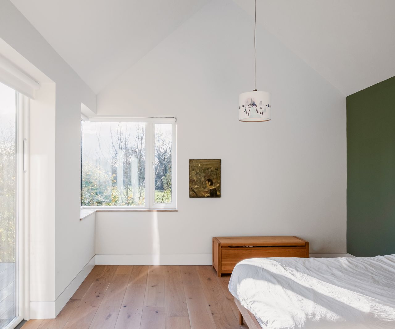 A bedroom with white walls and a green statement wall with plenty of natural light