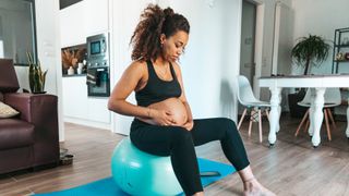 Pregnant women sitting on a yoga ball cradling her stomach