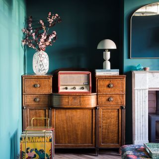 living room paint colours 2023, living room colour mistakes, living room with teal walls, vintage cabinet, retro theme, fireplace, mirror, vintage radio, vases, table lamp