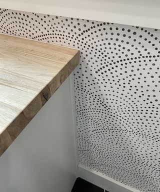 A close-up shot of white and black spotted wallpaper decor being pasted around a wooden desk