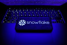 snowflake logo on smartphone sitting on laptop and blue binary code reflecting off both screens