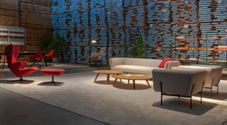Prostoria showroom interior with walls made of stacked wooden planks. On the foreground are a high-backed red armchair and ottoman and a sofa and armchair set in neutral colours