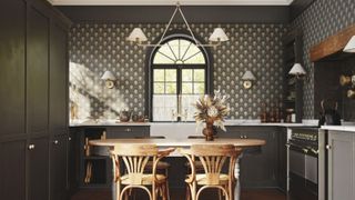 Dark and moody luxury kitchen with wooden dining table in foreground. There is art deco deep green wallpaper and dark green cabinets and white counters