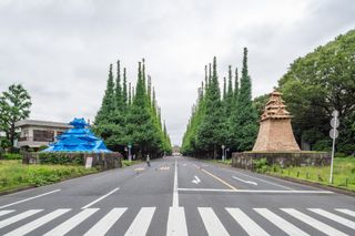 Standing in the centre of a dual carriageway with two traditional Japanese style castle street art on either side. The left is in blue and the right is in brick colour.