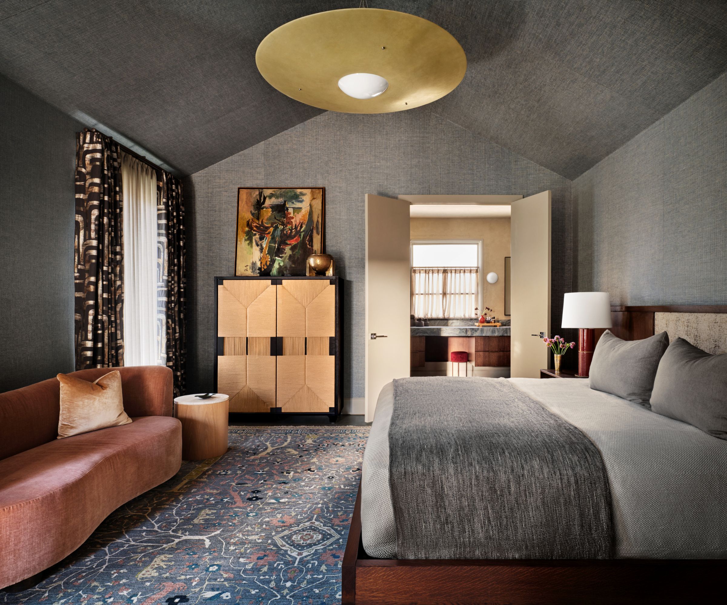 Bedroom with grey glasscloth walls, light grey bedding, patterned rug, pink velvet sofa