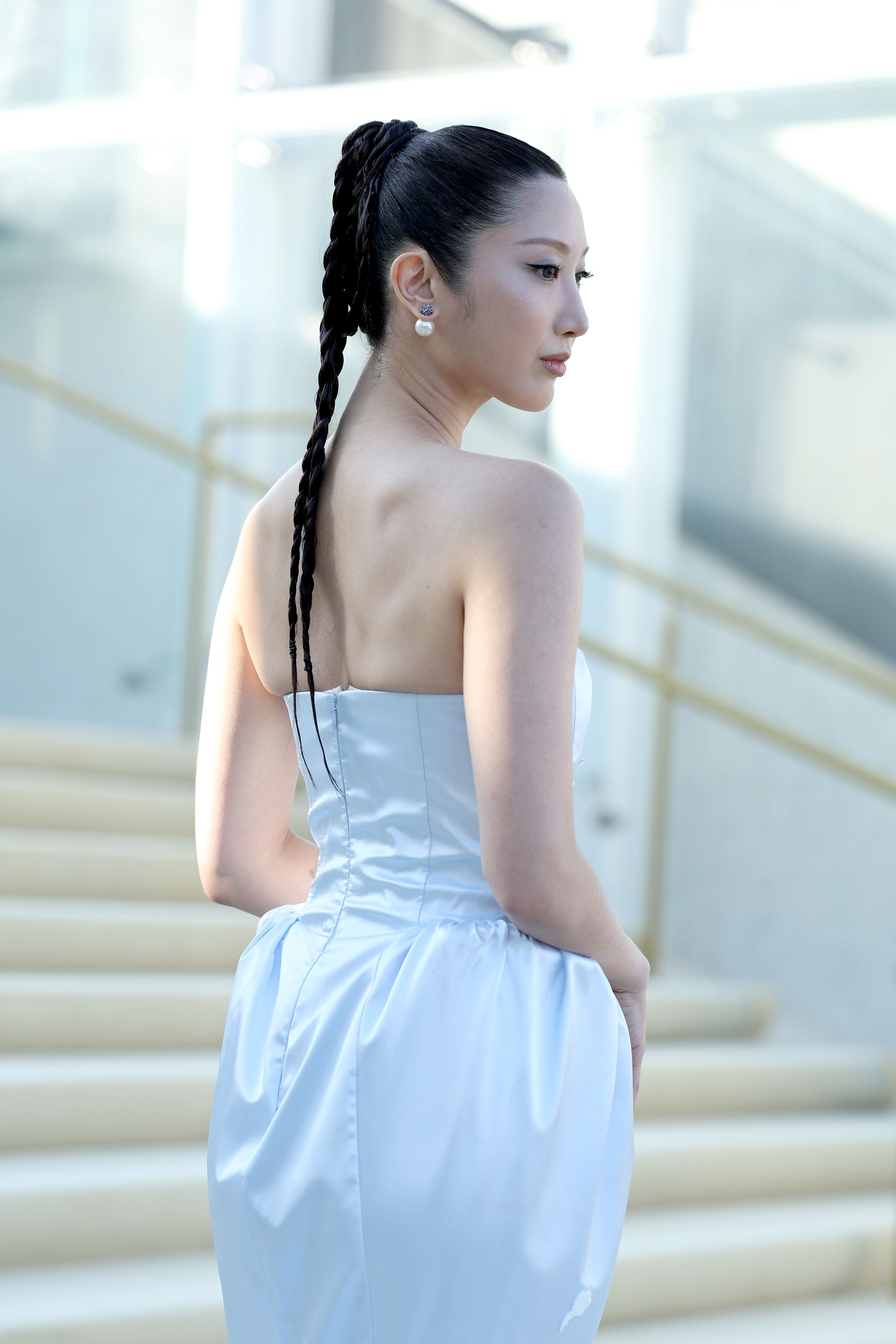 a woman wears a white gown and poses on a staircase with her back turned