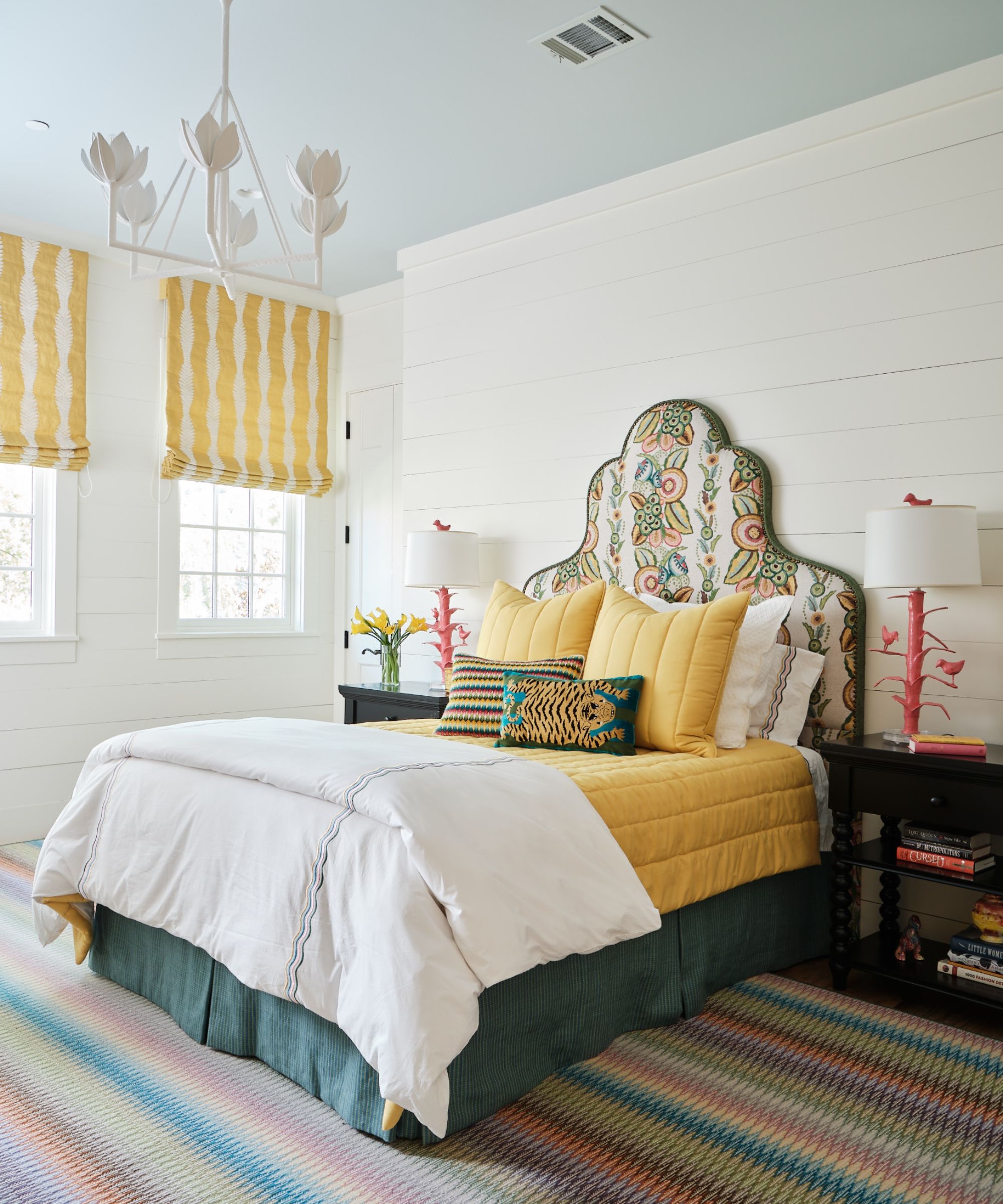 colorful kids bedroom with crisp white shiplapped walls, soft blue ceiling and colorful decor like striped carpet and an upholstered patterned headboard with a scheme of yellow and green on the bedding