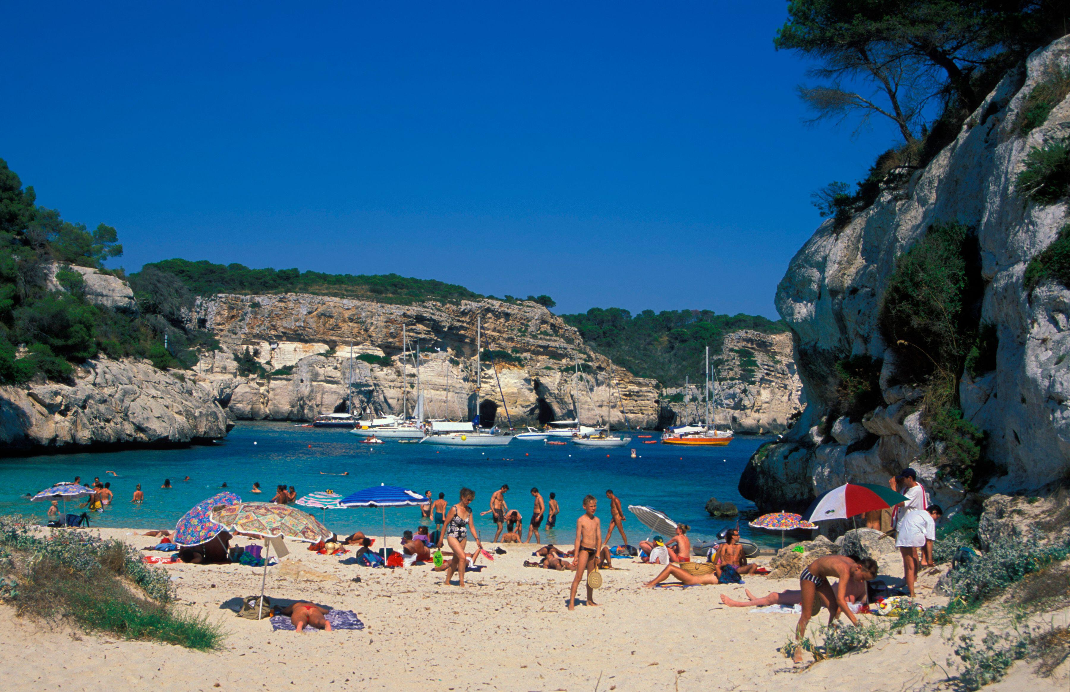 beach goers enjoy the water and sunshine at Cala Macarelleta beach in menorca