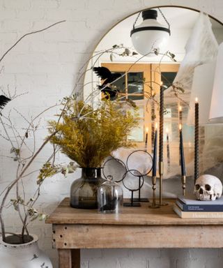 wooden console table with foliage and halloween decor with taper black candles, round mirror on wall