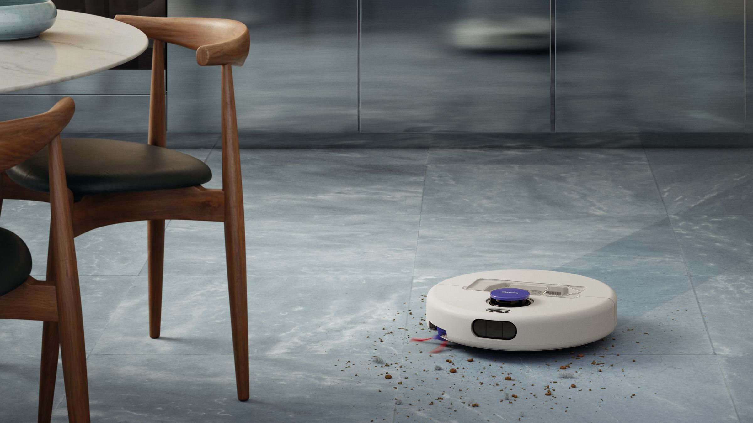 Dyson Nurovi robot vacuum vacuuming crumbs off grey floors next to a dining room table