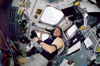 Astronaut Laurel Clark smiles for the photograph while situated on Columbia's aft flight deck near some large windows.