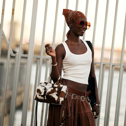 model standing in front of railings wearing a white tank and brown skirt