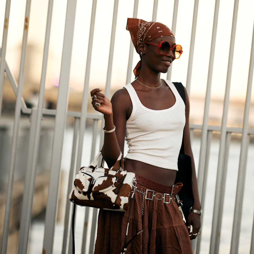 model standing in front of railings wearing a white tank and brown skirt