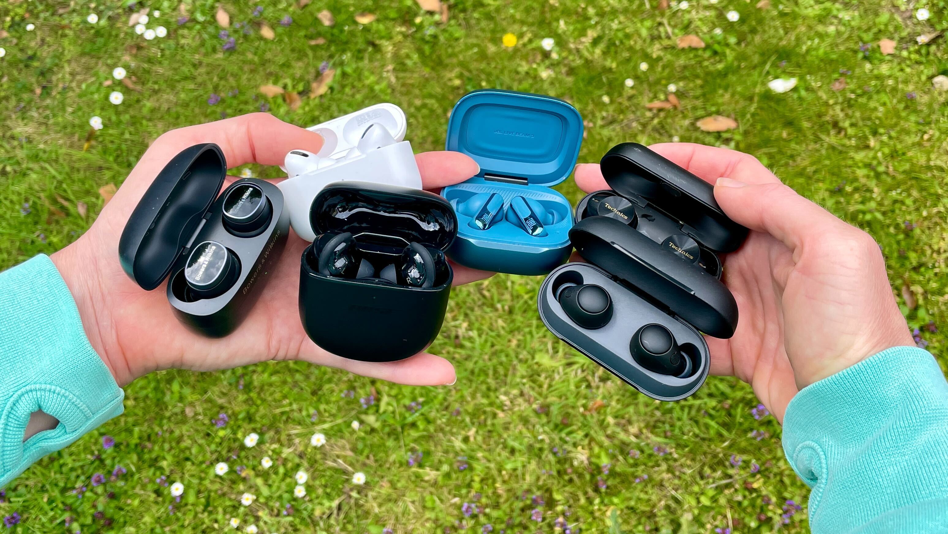 A woman's hands holds six pairs of earbuds, with grass in the background