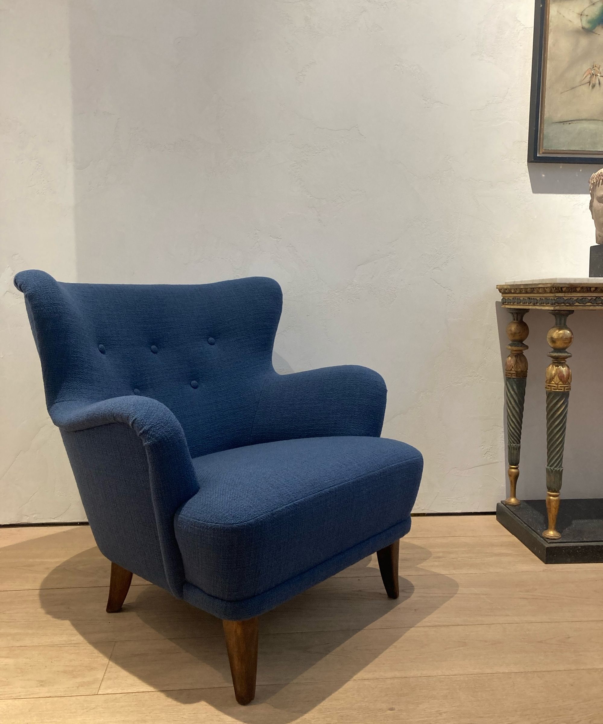 Midcentury blue upholstered armchair on a wooden floor beside a gilded console table