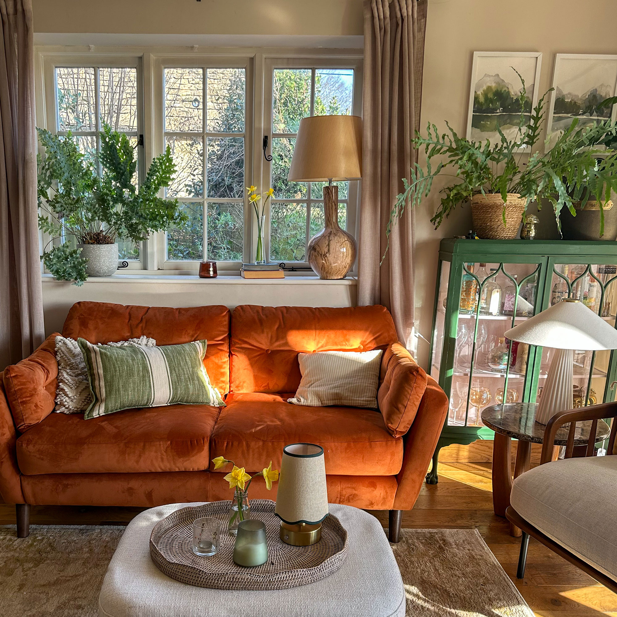 Living room with orange sofa, cream fabric ottoman as coffee table and green cabinet bar cart